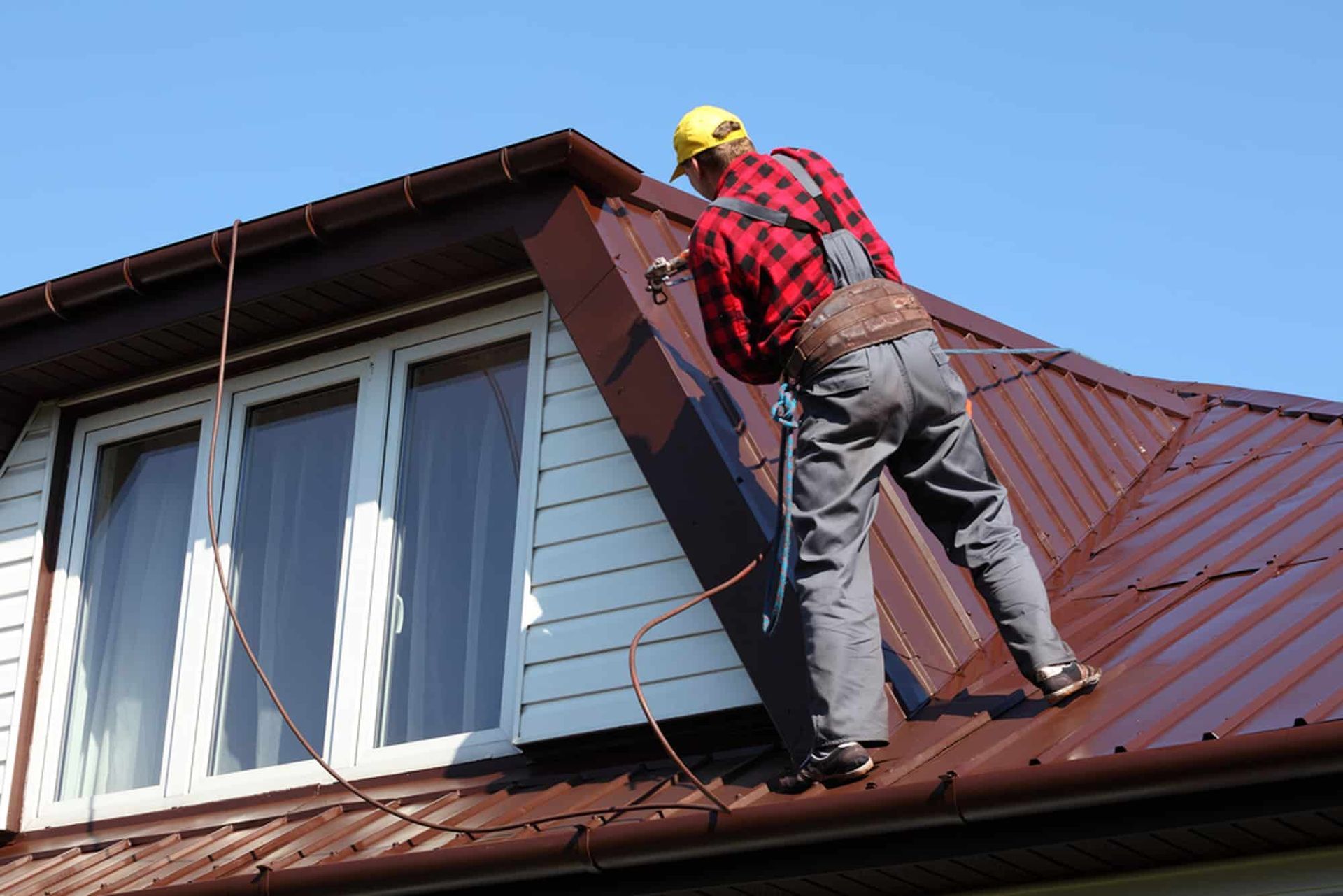 Man in Red Shirt and Yellow Hat on Brown Roof — Expert Plumbing & Solar Services Bathurst in Blayney, NSW