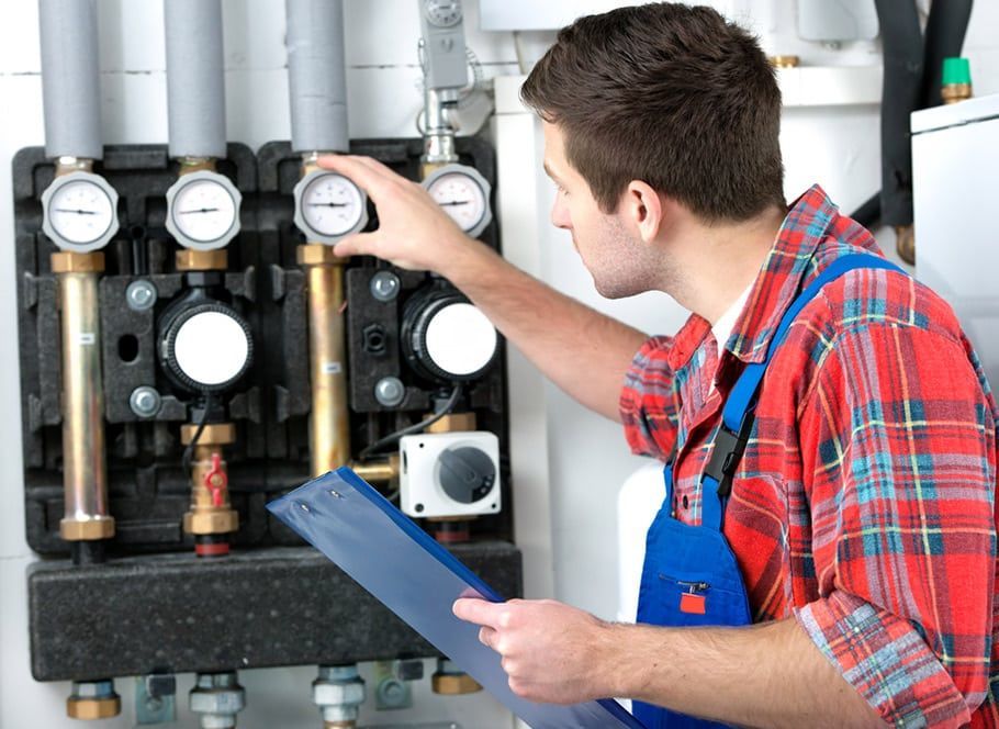 Plumber in Red Plaid Shirt and Blue Overalls Checks Gauges on Heating System — Expert Plumbing & Solar Services Bathurst in Kelso, NSW
