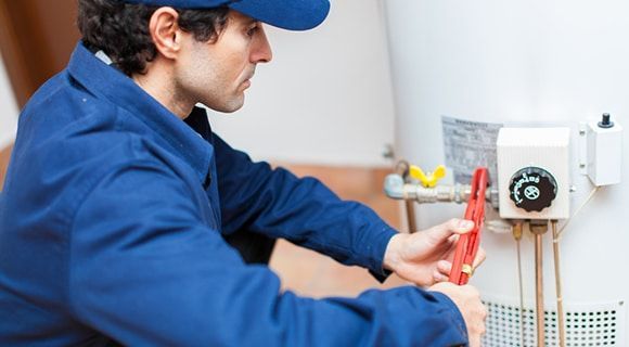 a Plumber in a Blue Uniform Working on a Water Heater — Expert Plumbing & Solar Services Bathurst in Blayney, NSW