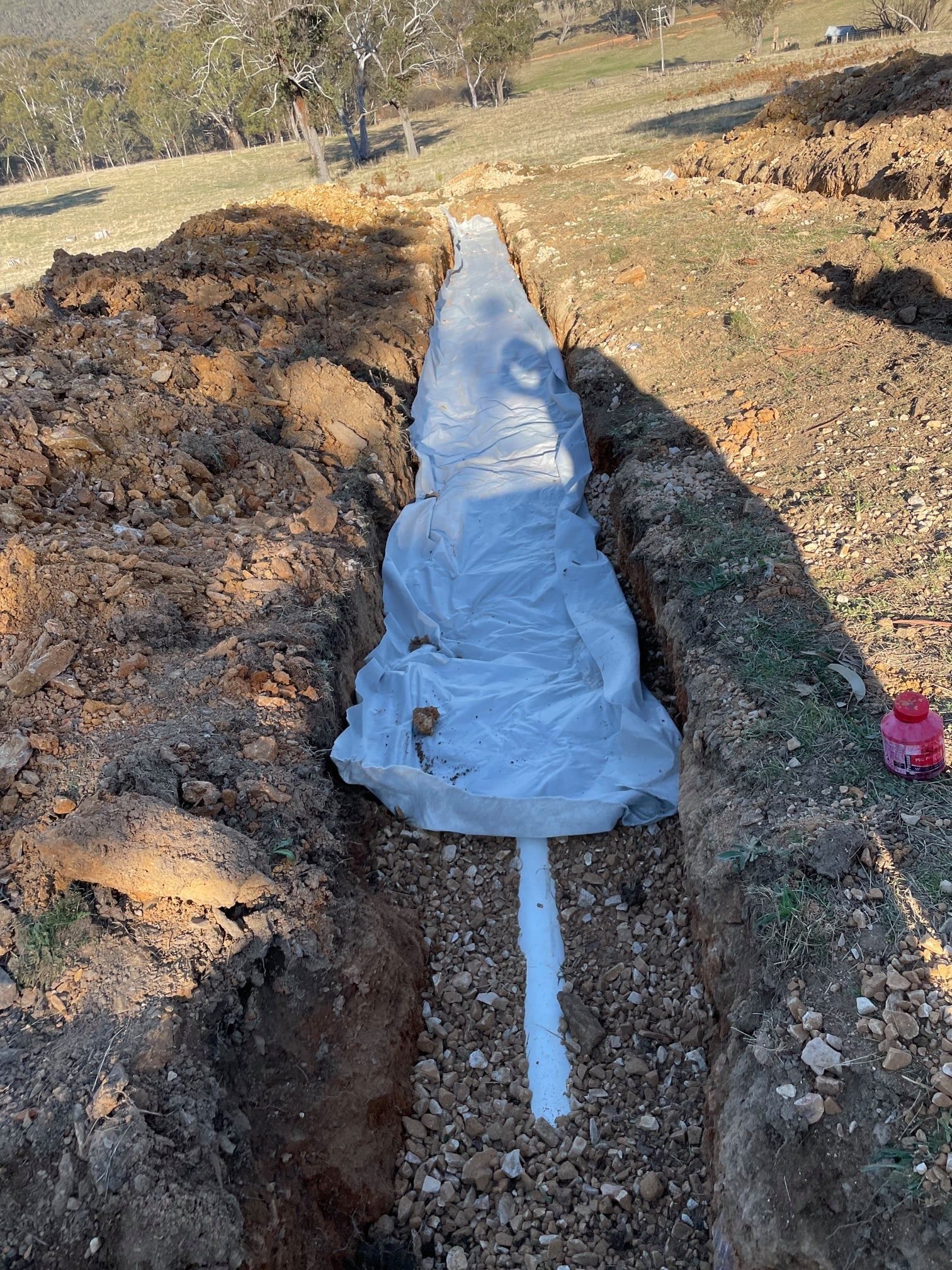 Long Narrow Trench in Dirt, With White Plastic and Pipe in the Center — Expert Plumbing & Solar Services Bathurst in Kelso, NSW
