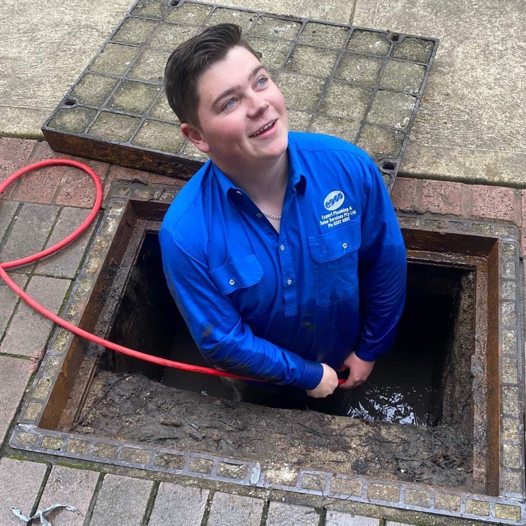 Man in Blue Uniform Looks Up From Open Sewer — Expert Plumbing & Solar Services Bathurst in Kelso, NSW