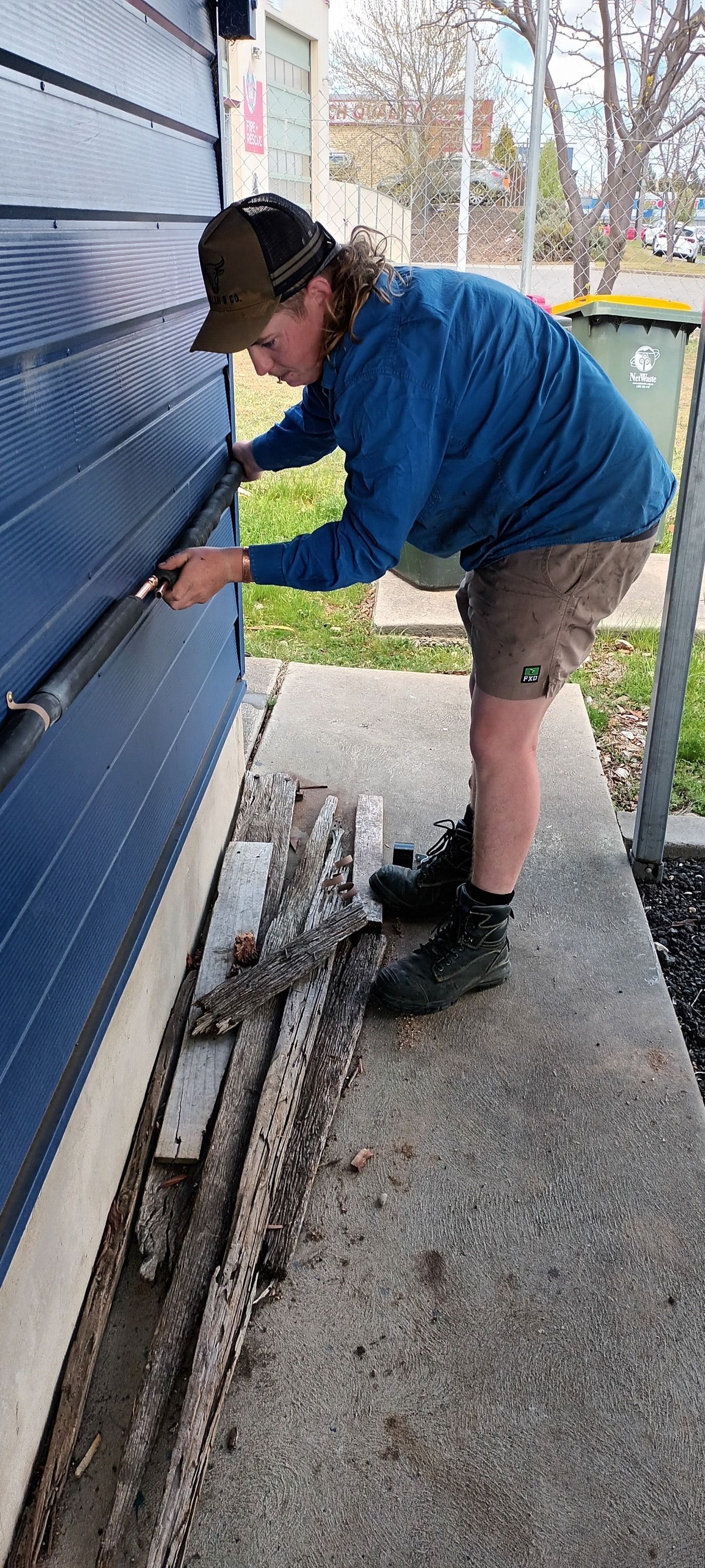a Person Repairs a Building's Blue Siding With a Tool — Expert Plumbing & Solar Services Bathurst in Kelso, NSW