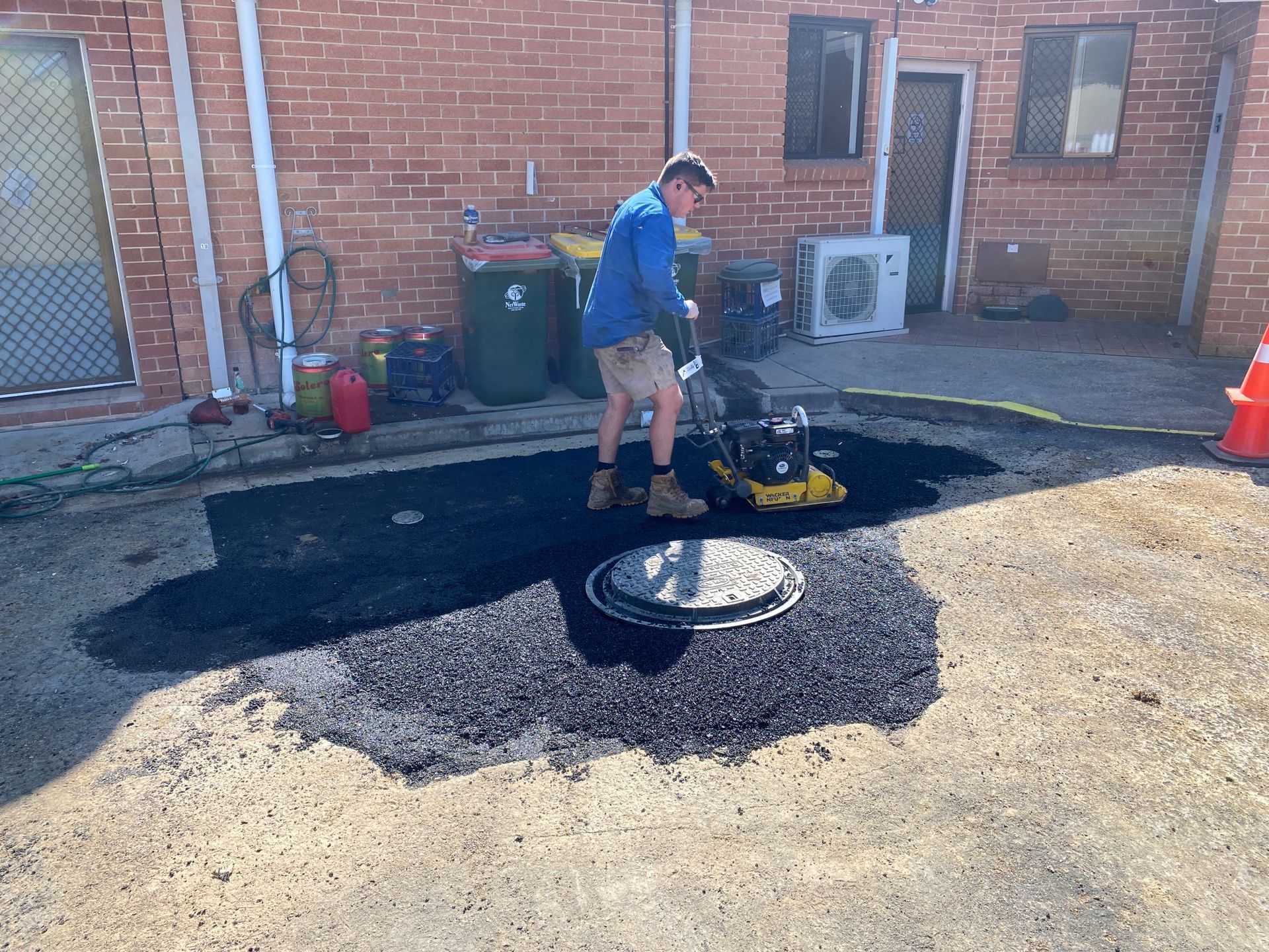 Man Compacting Asphalt Around a Manhole Cover With a Plate Compactor — Expert Plumbing & Solar Services Bathurst in Kelso, NSW