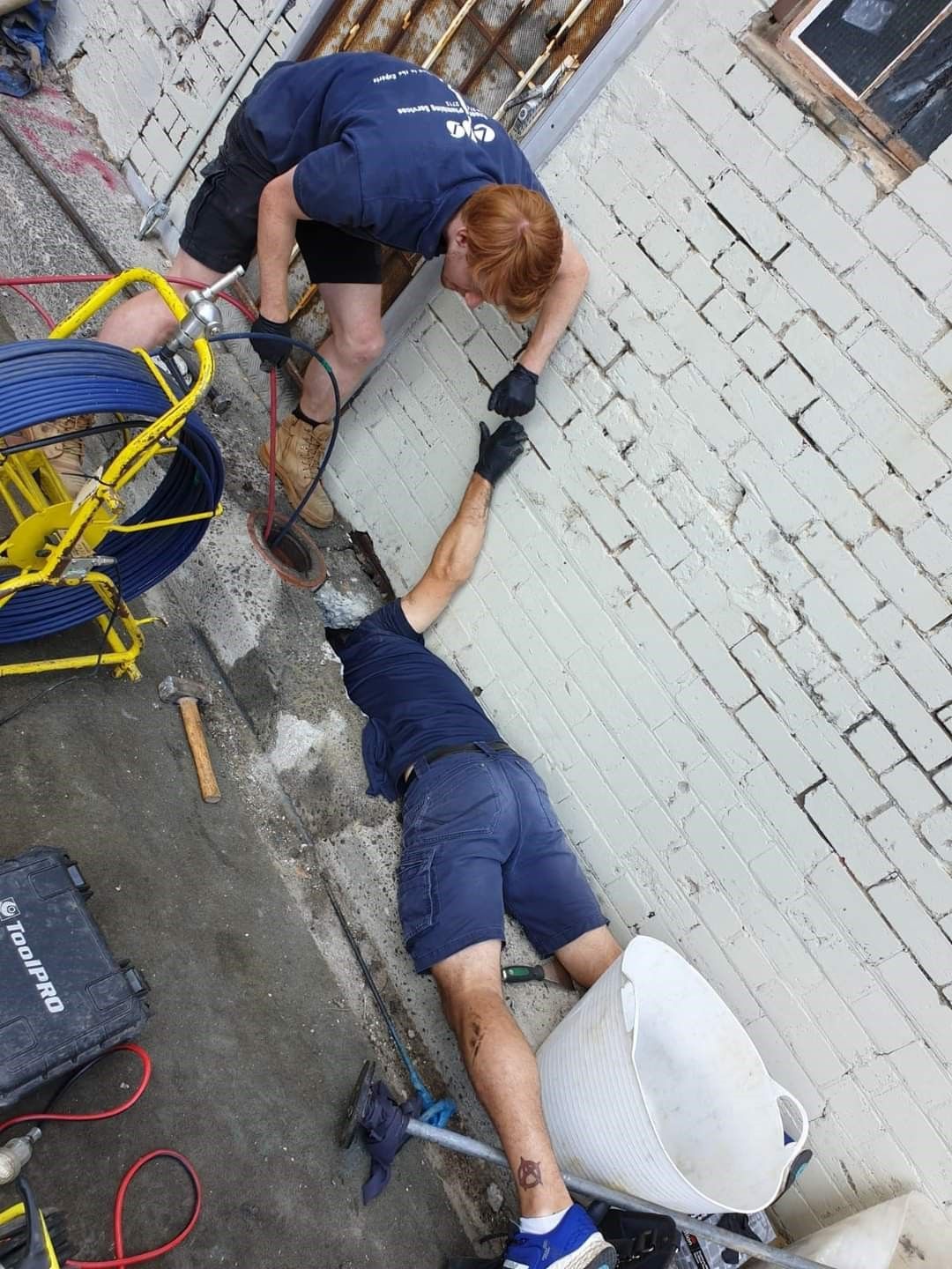 Two Workers Near a White Brick Wall — Expert Plumbing & Solar Services Bathurst in Kelso, NSW