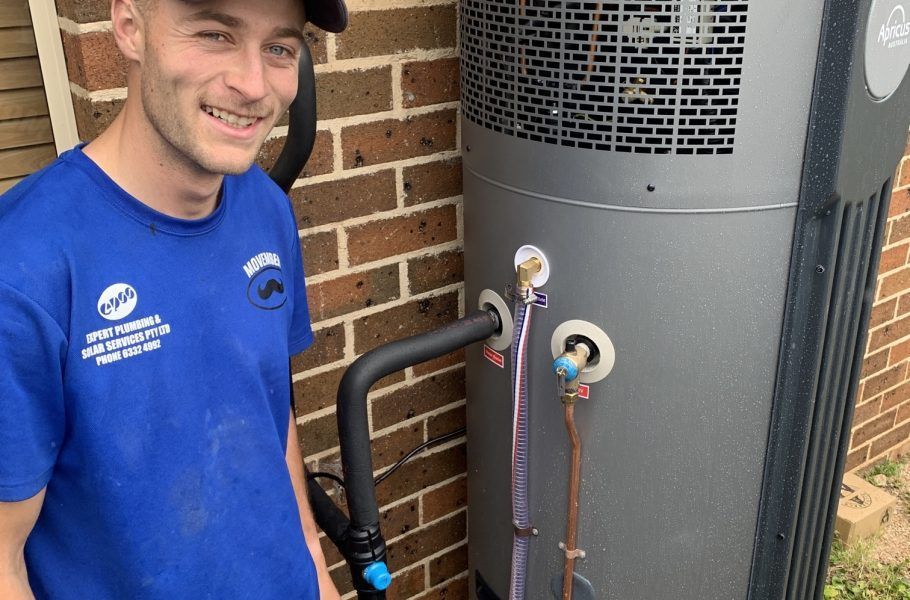 Man in Blue Shirt Smiles Next to a Heat Pump System — Expert Plumbing & Solar Services Bathurst in Kelso, NSW