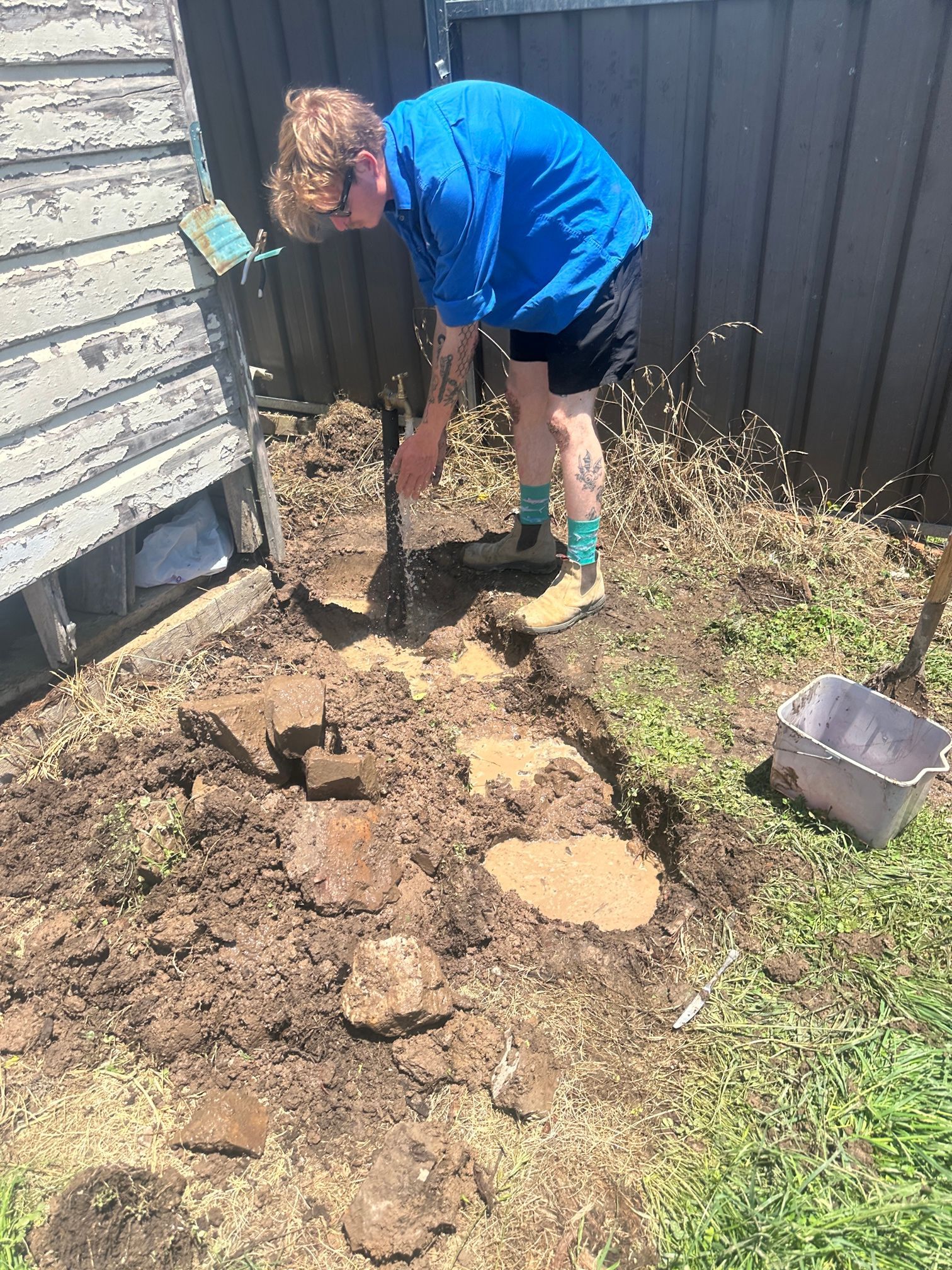 Person Digging in Dirt Near a Weathered Wooden Structure, Holding a Shovel — Expert Plumbing & Solar Services Bathurst in Kelso, NSW
