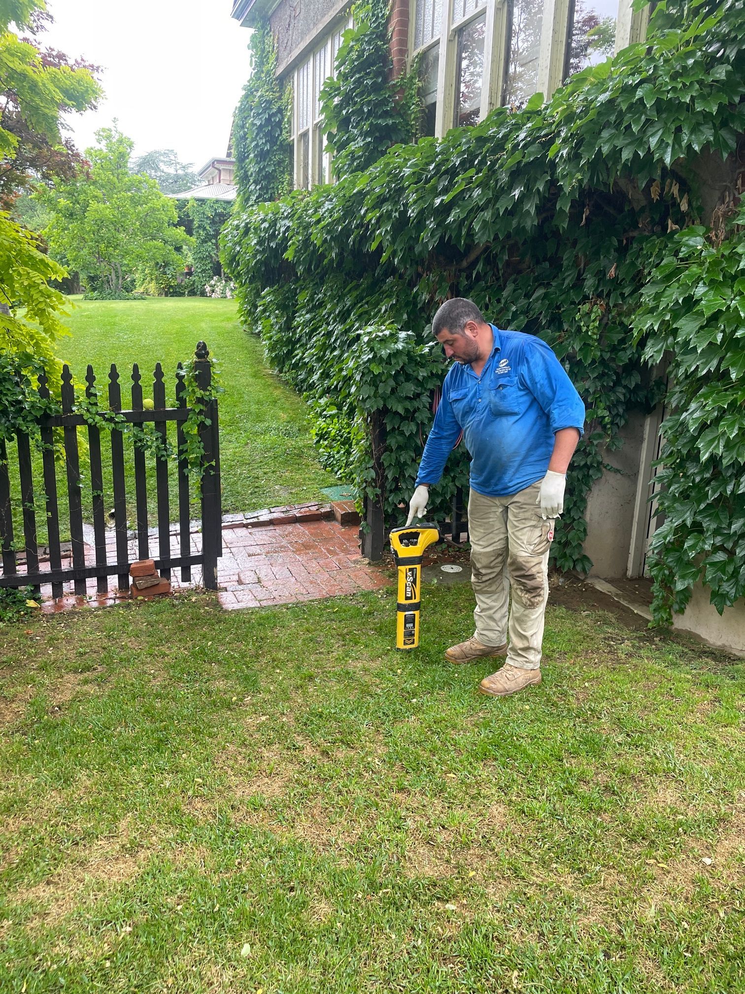 Man Using a Yellow Utility Locating Device on a Grassy Lawn — Expert Plumbing & Solar Services Bathurst in Orange NSW