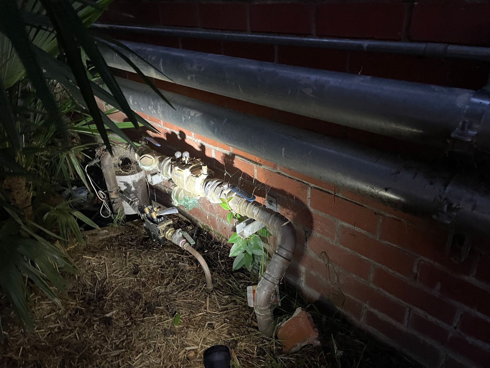 A Close-up of Outdoor Pipes and Valves Near a Brick Wall — Expert Plumbing & Solar Services Bathurst in Kelso, NSW