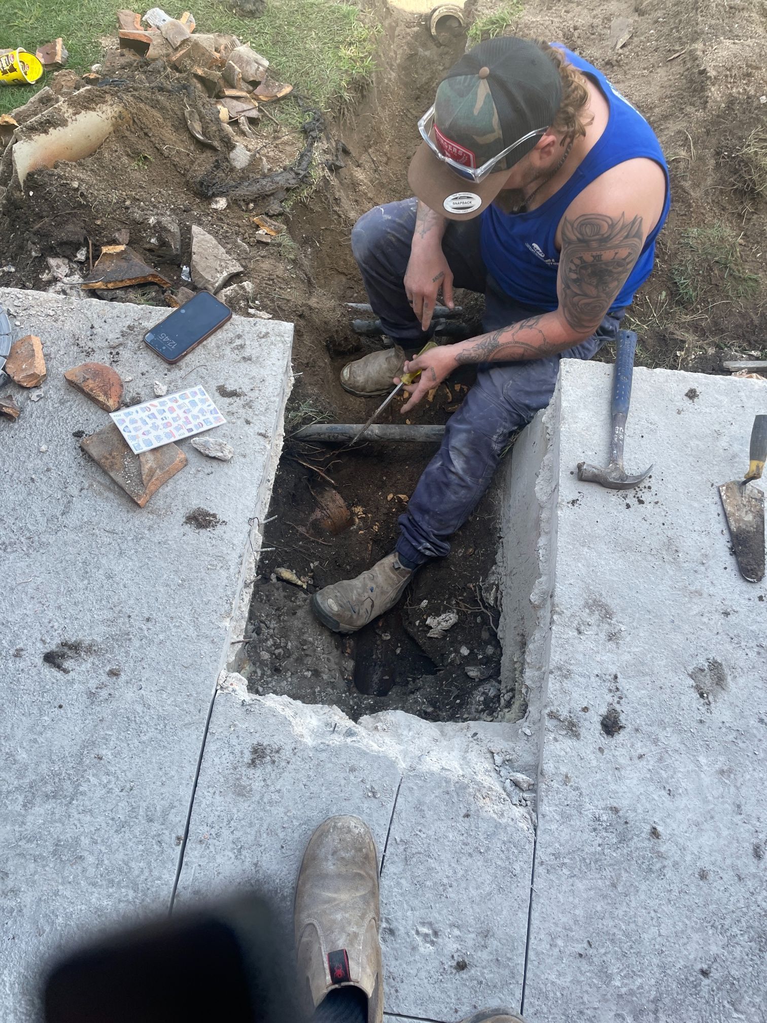 a Person Working on a Pipe in a Concrete Trench, Wearing a Tank Top — Expert Plumbing & Solar Services Bathurst in Blayney, NSW