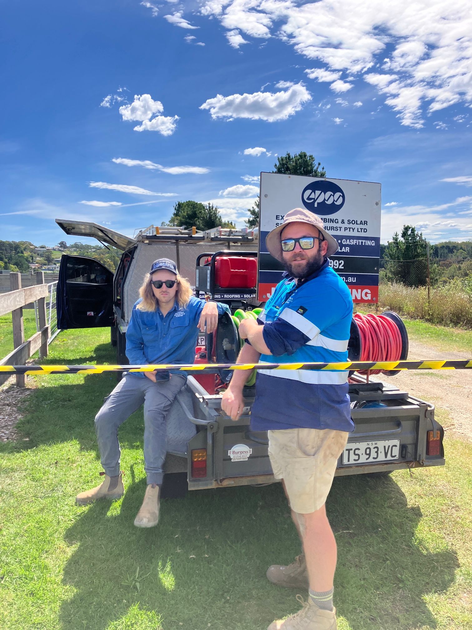 Two Workers Stand Near a Trailer and Truck in a Sunny Outdoor Setting — Expert Plumbing & Solar Services Bathurst in Kelso, NSW