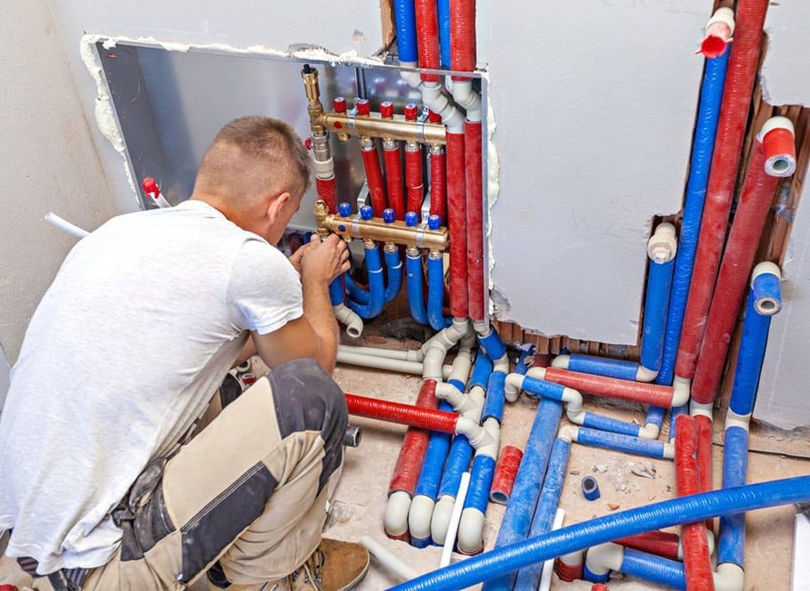Plumber Installing Radiant Heating Manifold With Red and Blue Pipes in Wall — Expert Plumbing & Solar Services Bathurst in Oberon, NSW