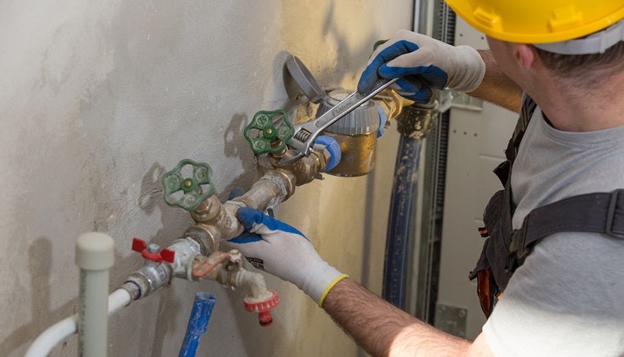 Plumber in Gloves and a Yellow Hard Hat Using a Wrench on Pipes — Expert Plumbing & Solar Services Bathurst in Kelso, NSW