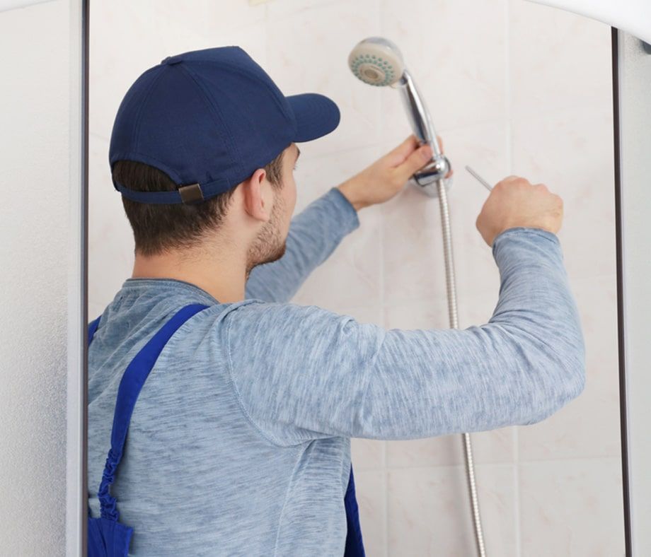 Person in a Blue Cap Installing Shower Head With a Screwdriver in a Bathroom — Expert Plumbing & Solar Services Bathurst in Oberon, NSW