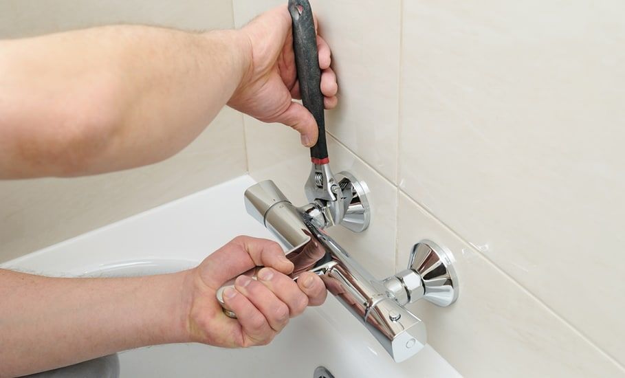 Person Using Wrench to Install or Repair a Chrome Faucet in a Bathtub — Expert Plumbing & Solar Services Bathurst in Kelso, NSW
