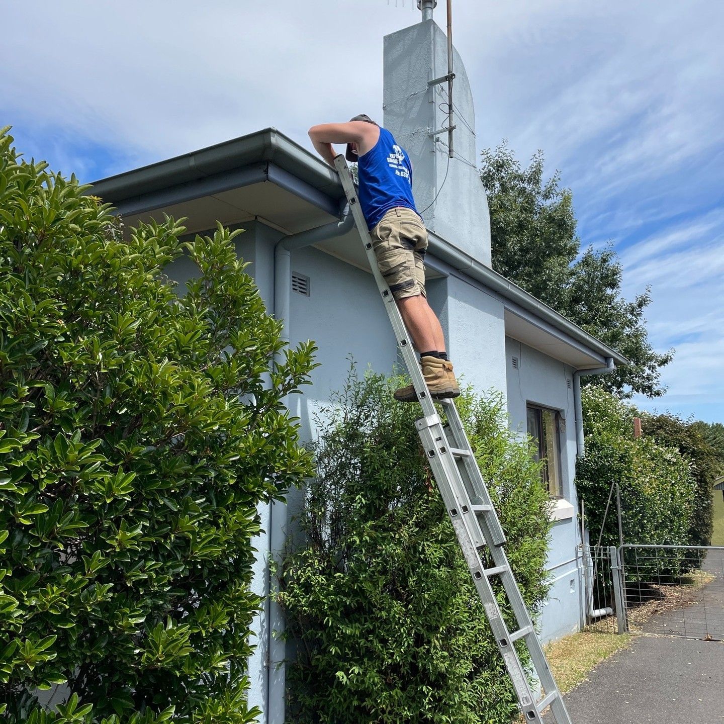 Person on Ladder Near Chimney, Reaching Toward Roof — Expert Plumbing & Solar Services Bathurst in Orange, NSW