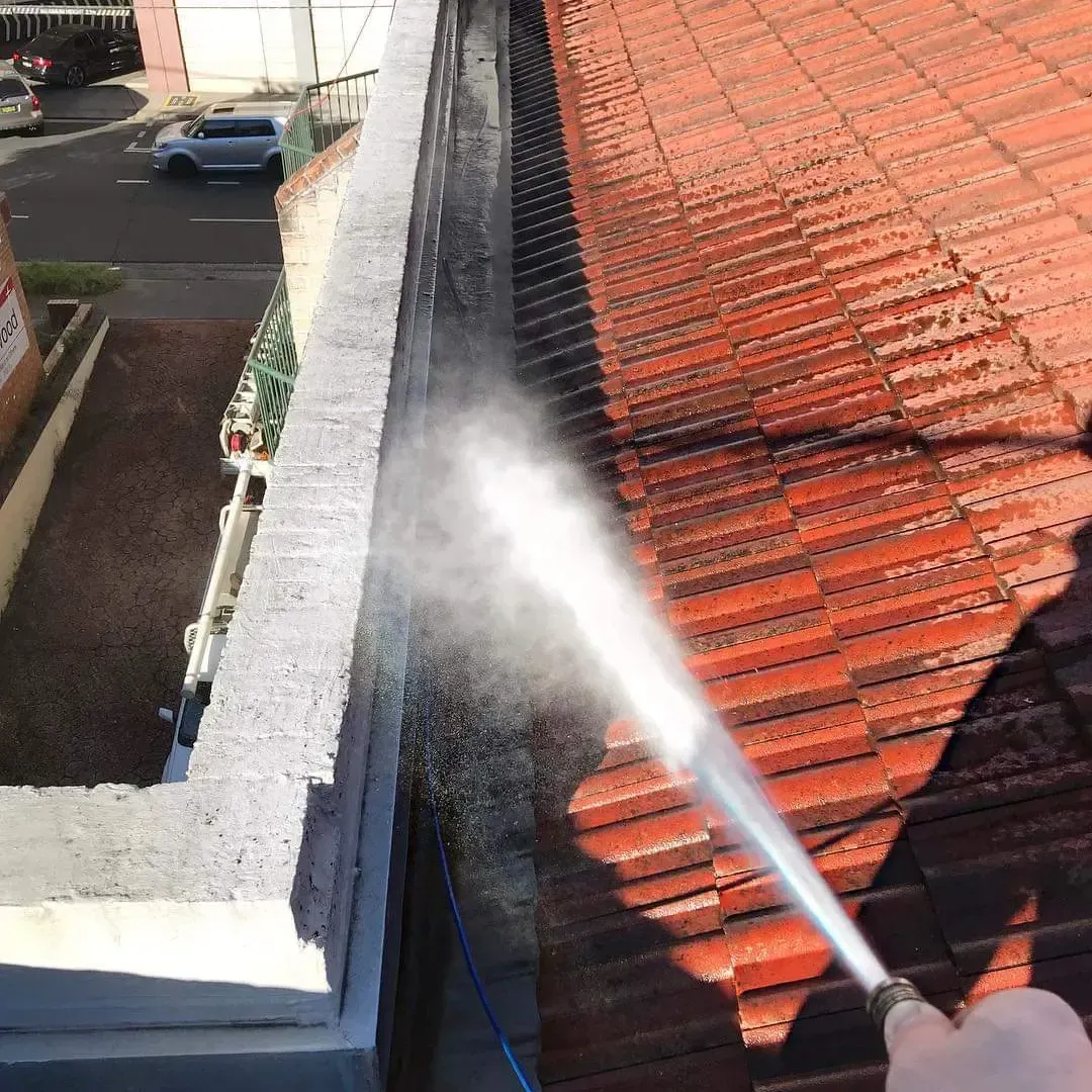 A Person Power Washing a Red Tile Roof and Gutter on a Sunny Day — Expert Plumbing & Solar Services Bathurst in Kelso, NSW