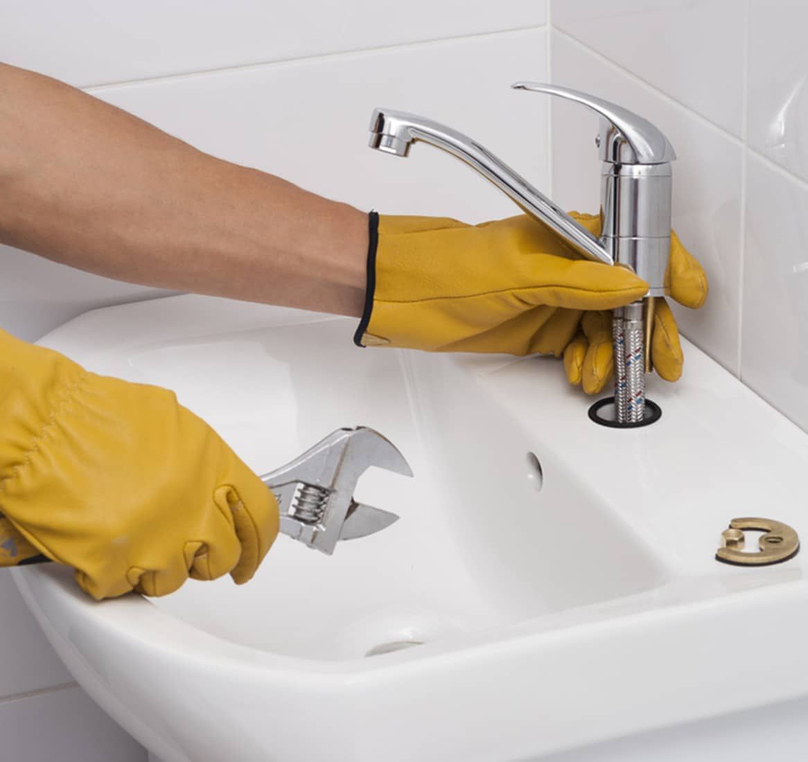 Person Wearing Yellow Gloves Uses a Wrench to Tighten a Faucet in a White Sink — Expert Plumbing & Solar Services Bathurst in Lithgow, NSW