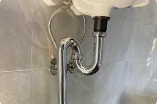 A Chrome P-trap Plumbing Fixture Attached to the Underside of a Bathroom Sink — Expert Plumbing & Solar Services Bathurst in Kelso, NSW
