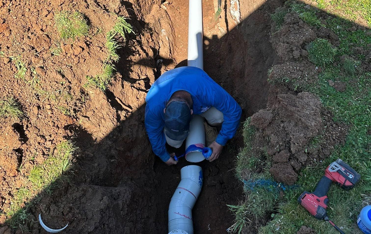Person in Blue Shirt Connecting Pvc Pipes in a Trench — Expert Plumbing & Solar Services Bathurst in Kelso, NSW