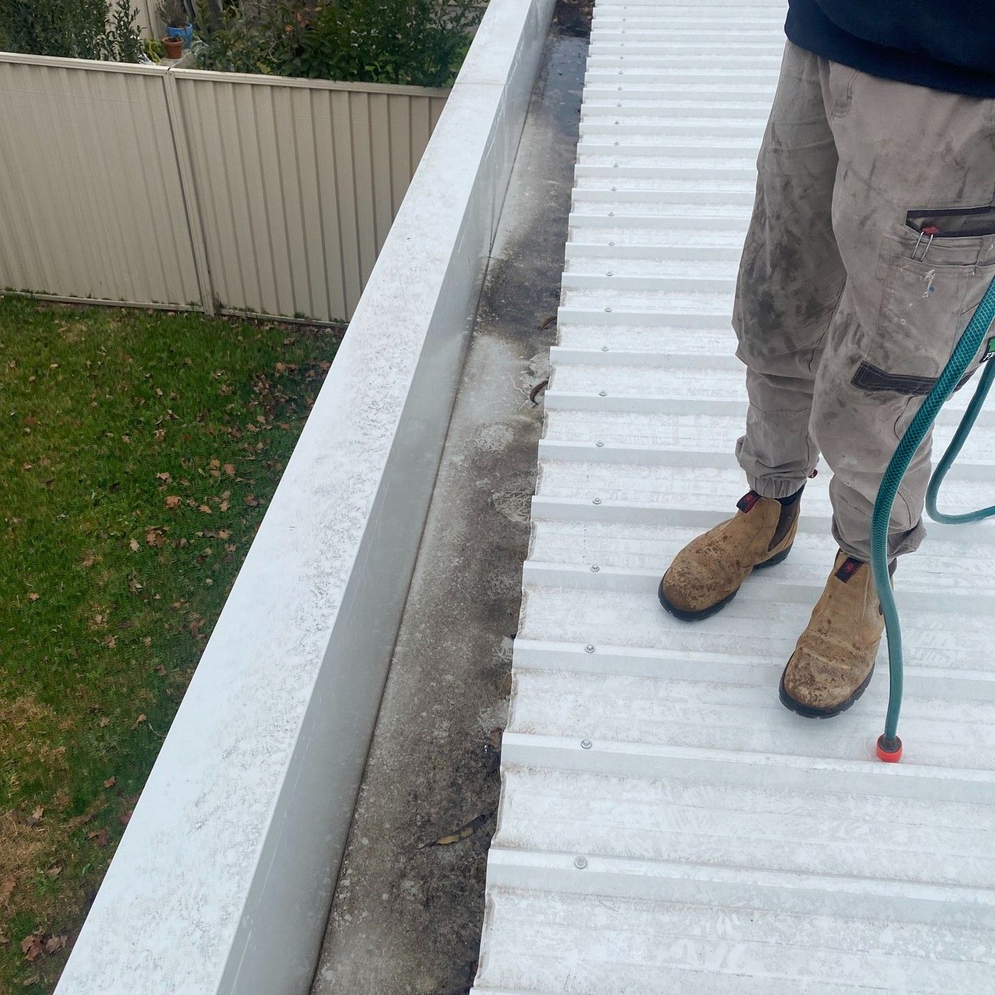 Person in Work Clothes Cleaning a White Metal Roof Next to a Gutter — Expert Plumbing & Solar Services Bathurst in Kelso, NSW