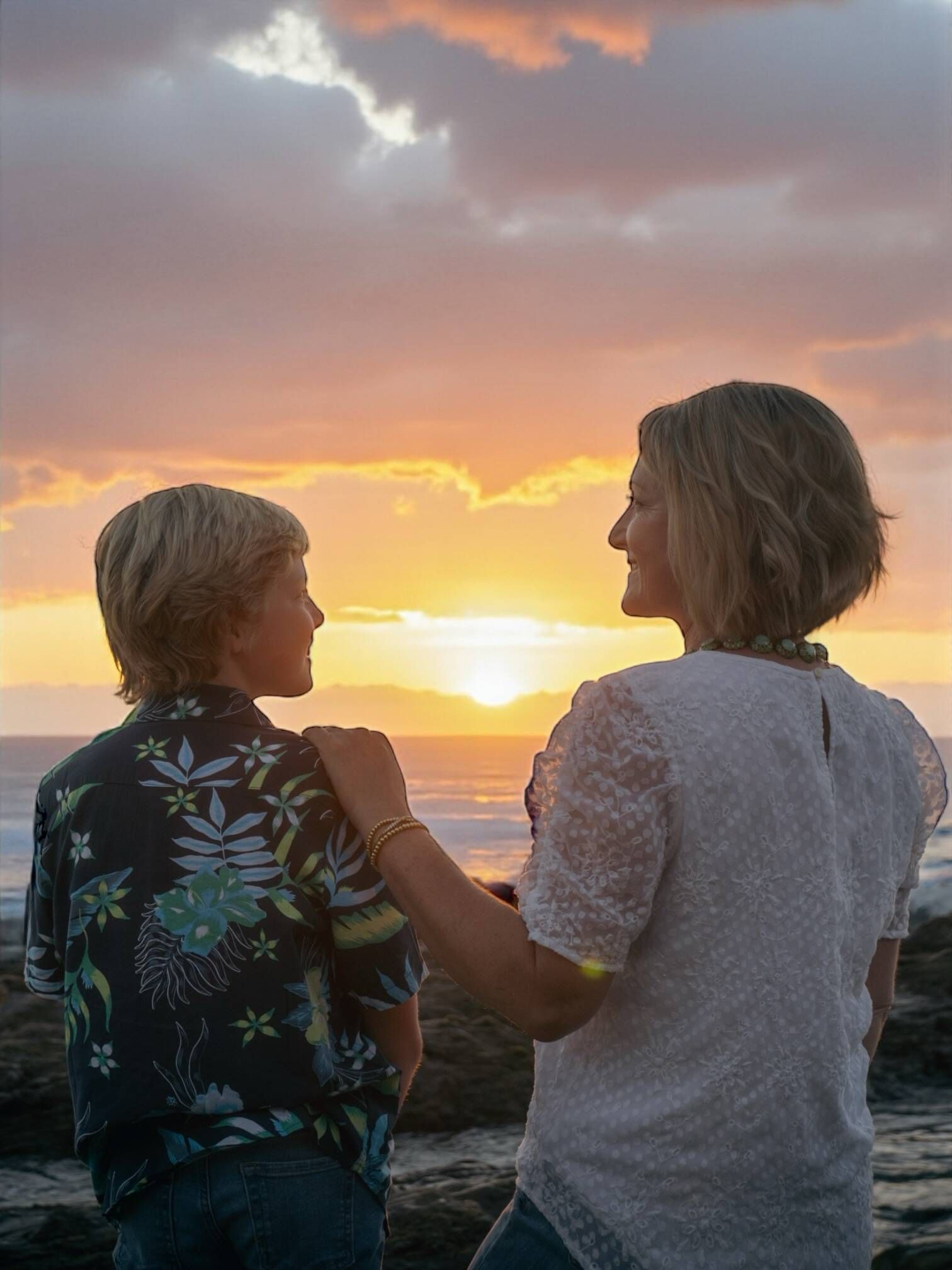 Woman with arm around boy's shoulder, watching sunset over ocean Jelena's Photo.