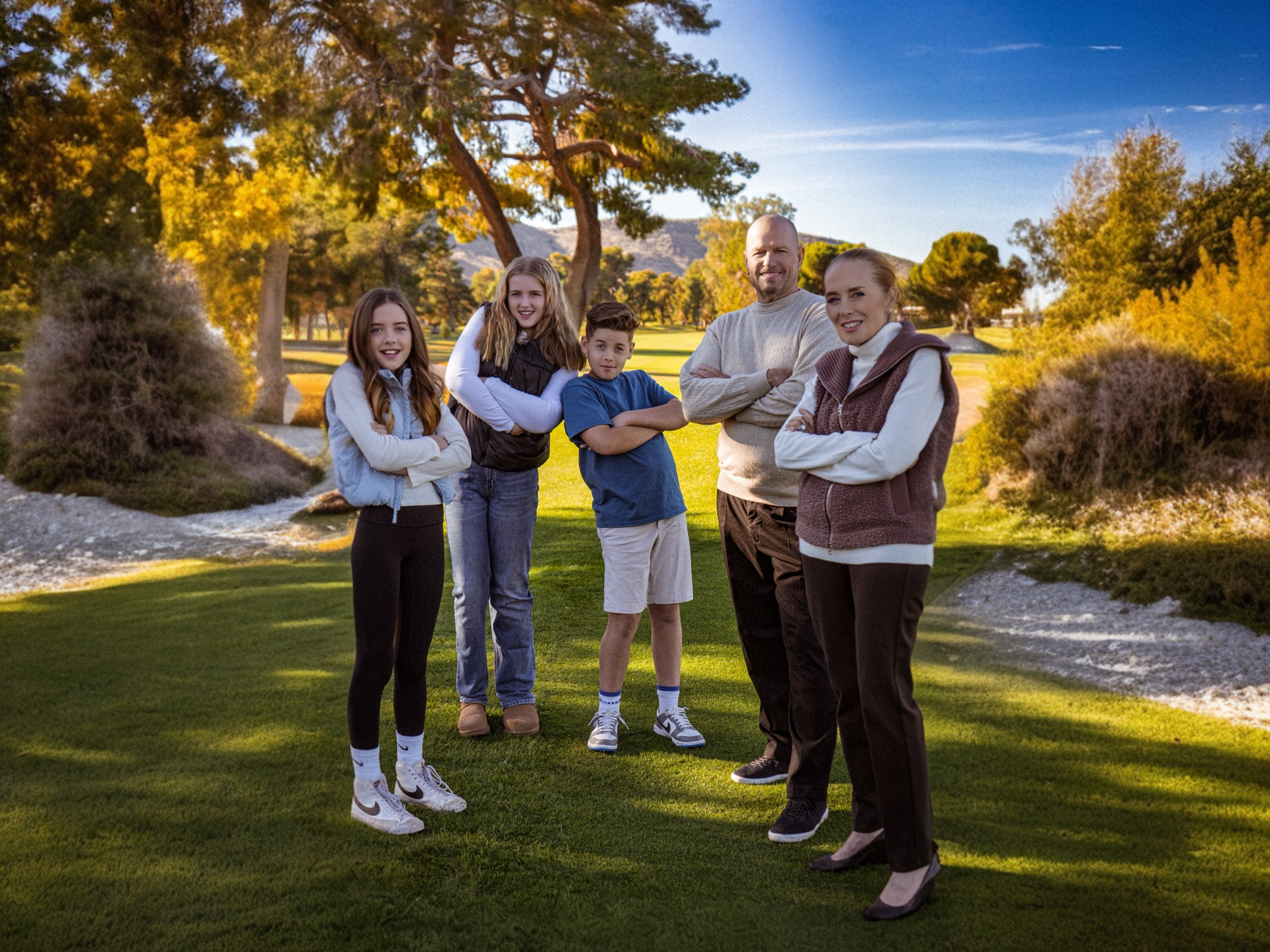 Family poses on a golf course, arms crossed. Sunny day, green grass, fall foliage by Jelena's Photo.