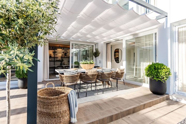 Outdoor patio with wicker dining set, white awning, and sliding glass doors beside a pool.