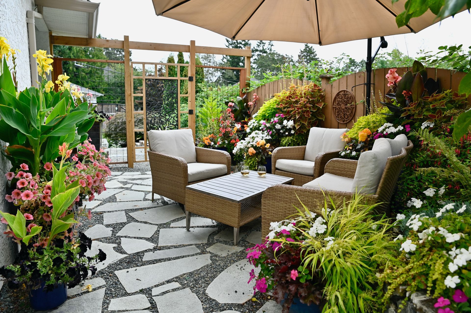 Cozy patio garden with wicker chairs, coffee table, and colorful flowers under a beige umbrella