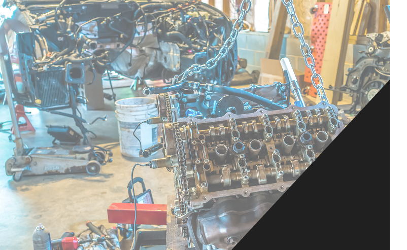 Engine being lifted in a garage, part of a car disassembled in the background. | Autoplex Auto Service