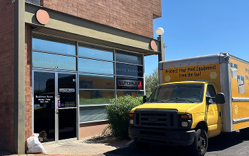 Yellow delivery truck parked outside a building with glass garage-style doors. | Autoplex Auto Service