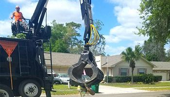 a man is standing on top of a garbage truck with a crane attached to it .