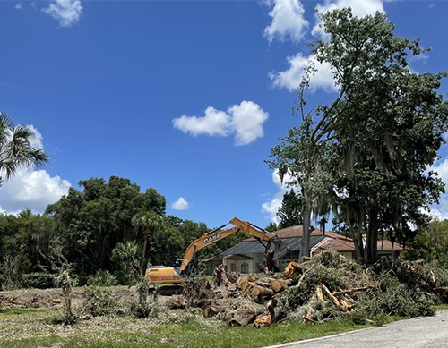 a case excavator is working on a pile of logs in front of a house