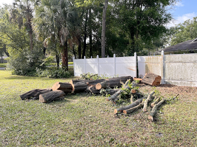 a pile of logs in a yard next to a white fence