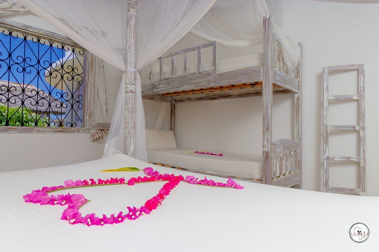 White bedroom with canopy bunk bed, window, ladder, and pink heart-shaped petals on the bed