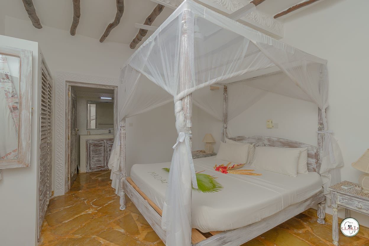 White canopy bed in a bright rustic bedroom with wood floor and open doorway