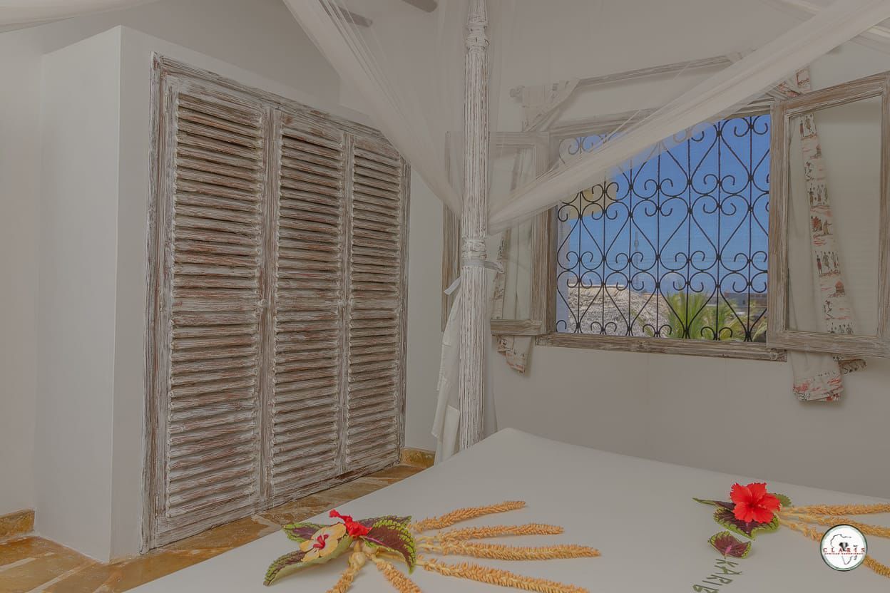 White bedroom with wooden wardrobe, bed, and window overlooking the sea.