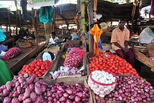 Bustling market stall with piles of tomatoes, onions, and other vegetables on display