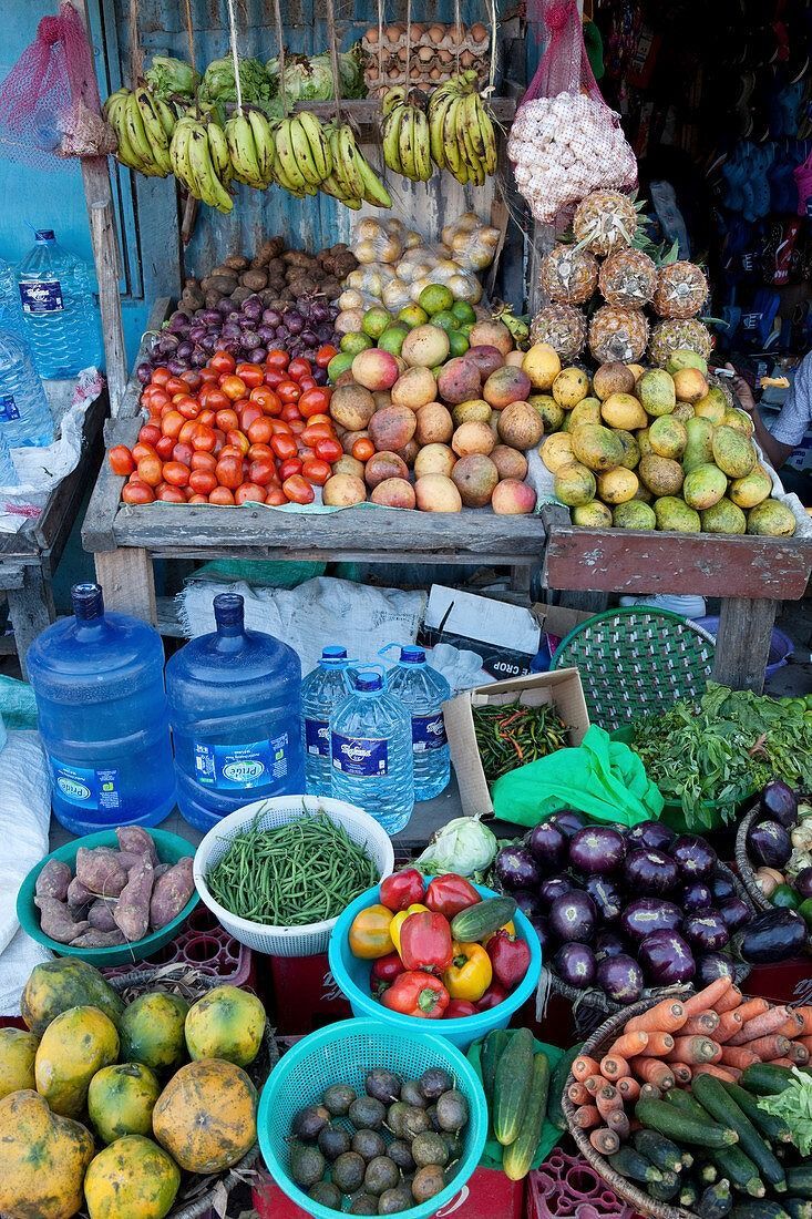 Colorful fruit and vegetable market stall with stacked produce and blue water jugs