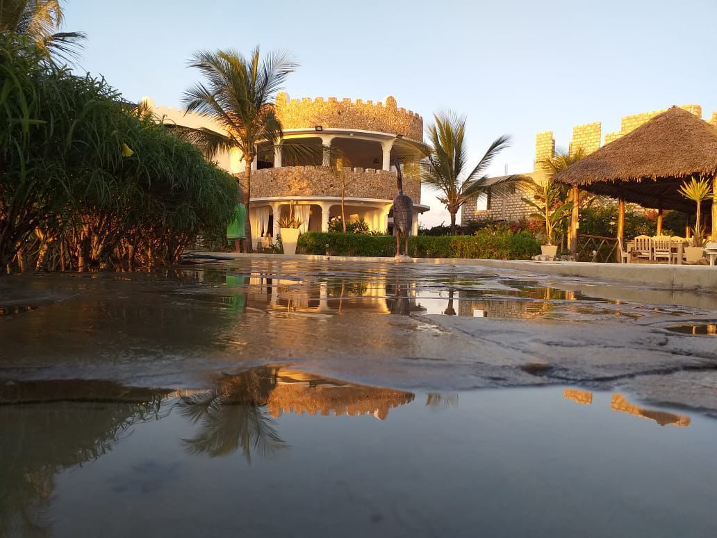 Tropical resort with thatched huts and palm trees reflected in a shallow water pool at sunset