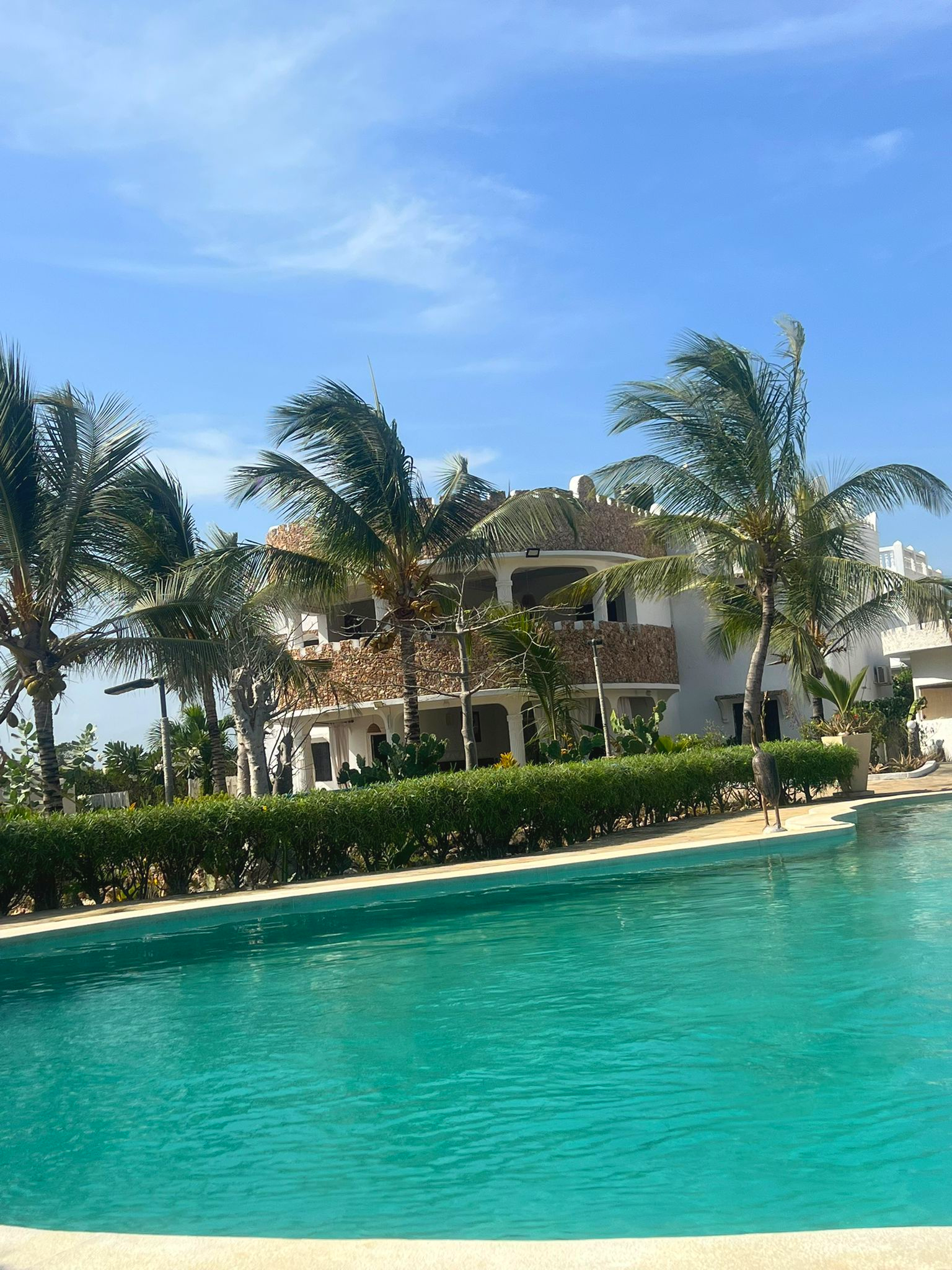 Tropical resort pool with turquoise water, palm trees, and a white villa under a clear blue sky