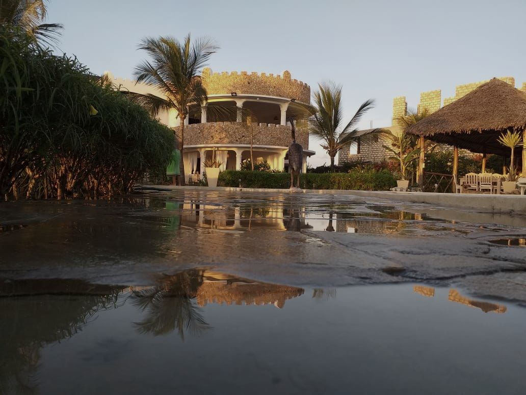 Thatched resort buildings reflected in a shallow pool at sunset