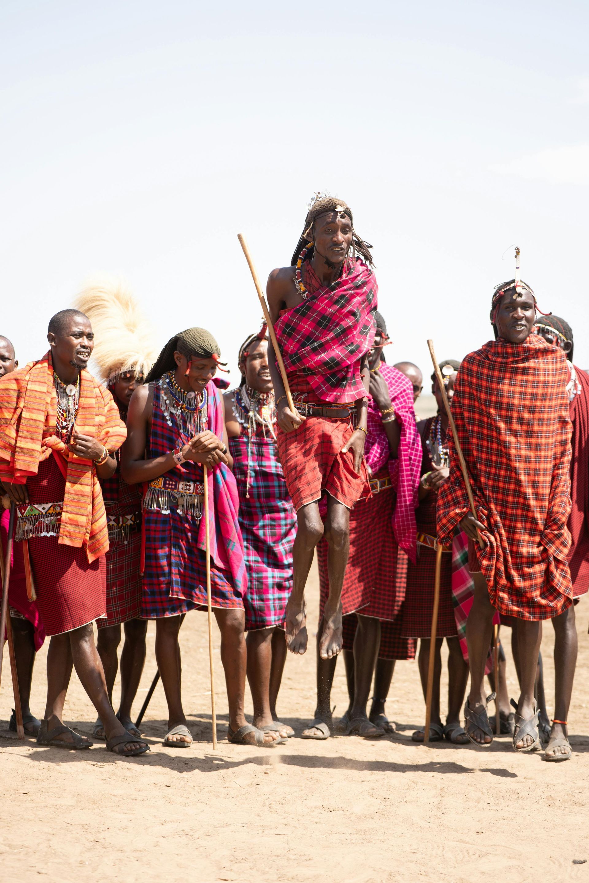 Group of people in bright traditional garments standing outdoors on a sandy plain under a clear sky