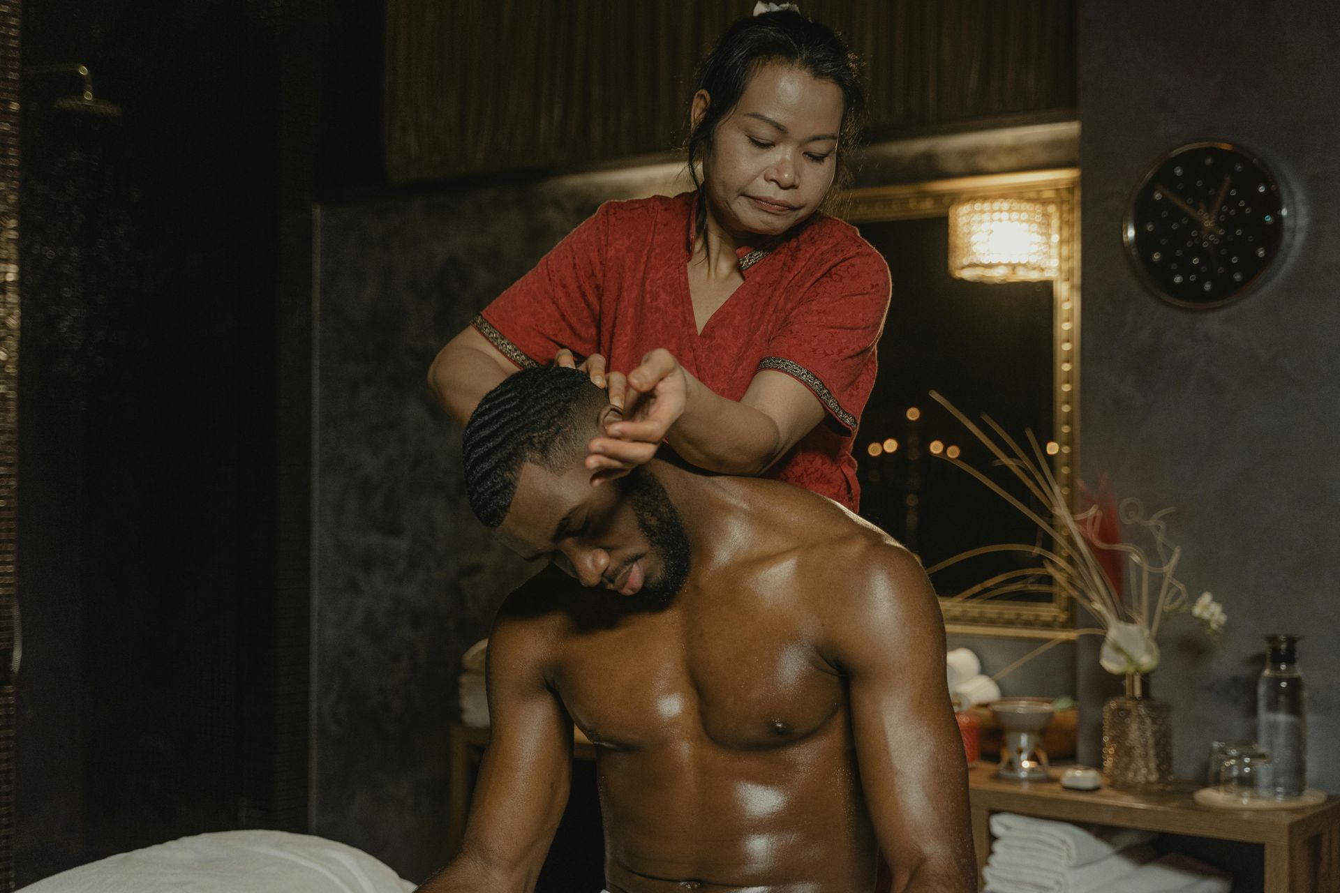 Person gives a shoulder massage in a dimly lit room with candles and a table in the background
