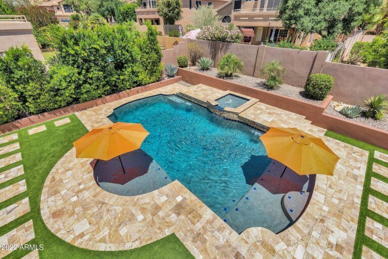 A pool area with orange umbrellas, a hot tub, and surrounding landscaping; aerial view.