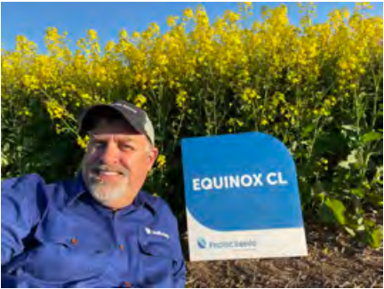 Man smiling beside blue EQUINOX CL sign in front of yellow flowering bushes