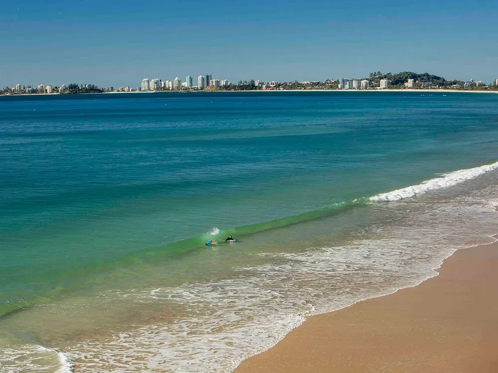A Person is Riding a Wave on a Beach With a City in the Background — O'Grady's Transport & Removals in Tweed Heads, NSW