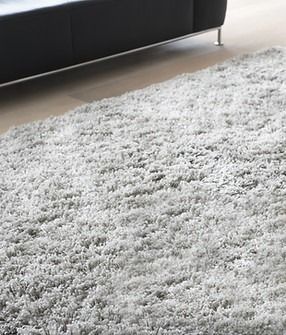 A gray rug is sitting on a wooden floor next to a black couch.
