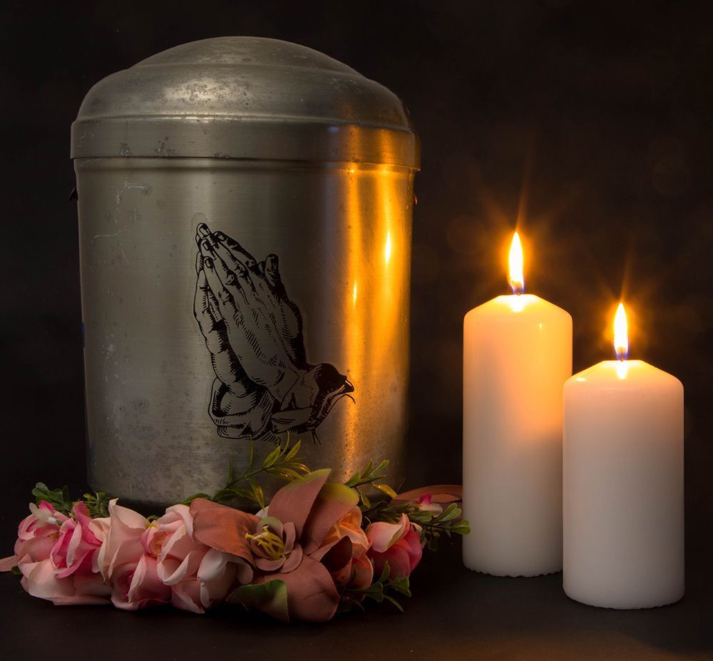 Cremation urn with pink roses, two light candles with focus on the detail of the cremation urn