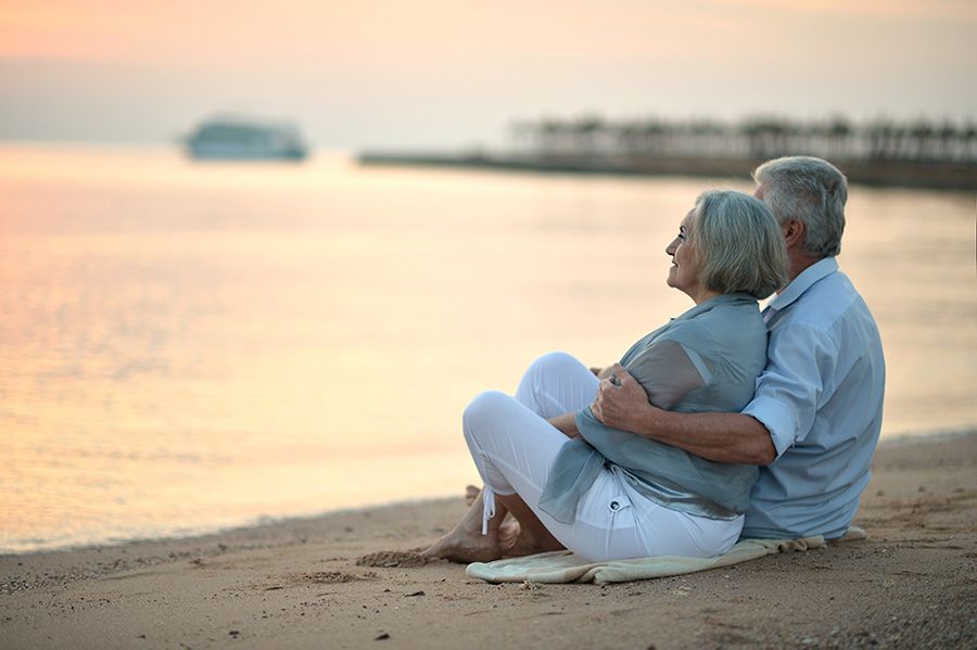 Elderly couple sitting on beach enjoying sunset