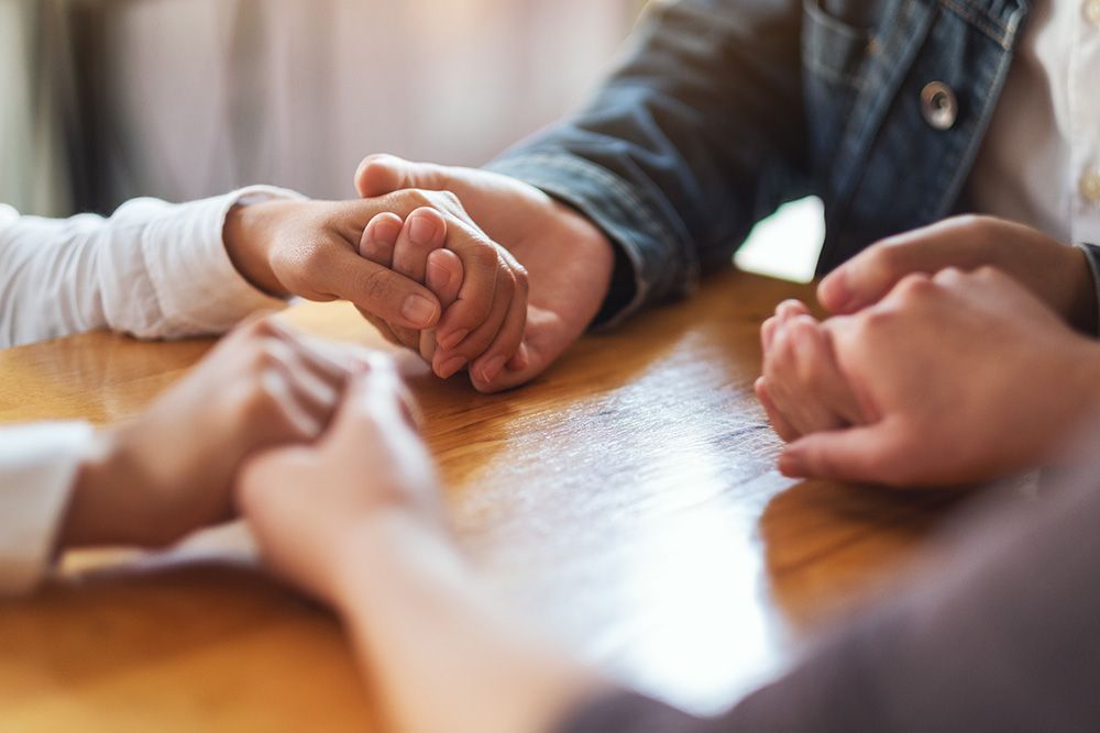 people at table holding hands supporting each other through grief with focus on hands